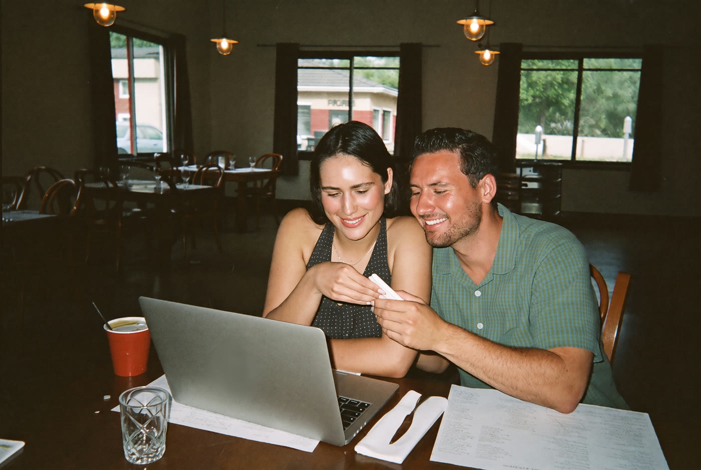 Husband and wife restaurant owners smiling together at a laptop in their dining room before opening