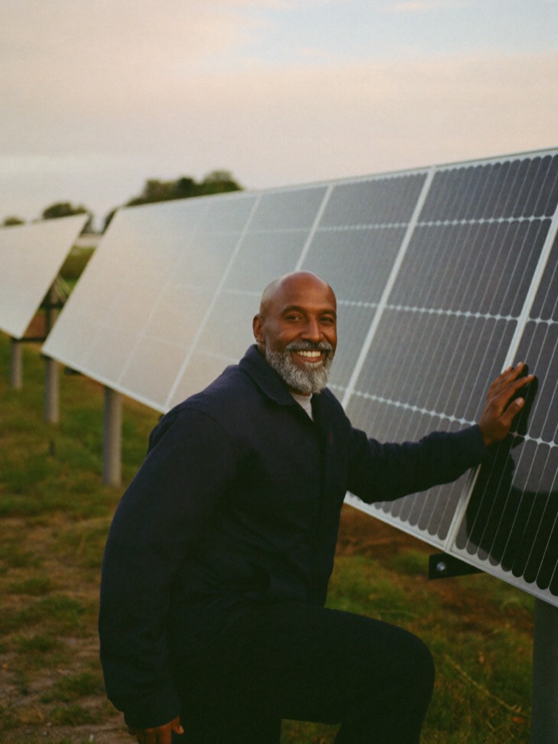 Solar company owner kneeling beside a row of solar panels at sunset